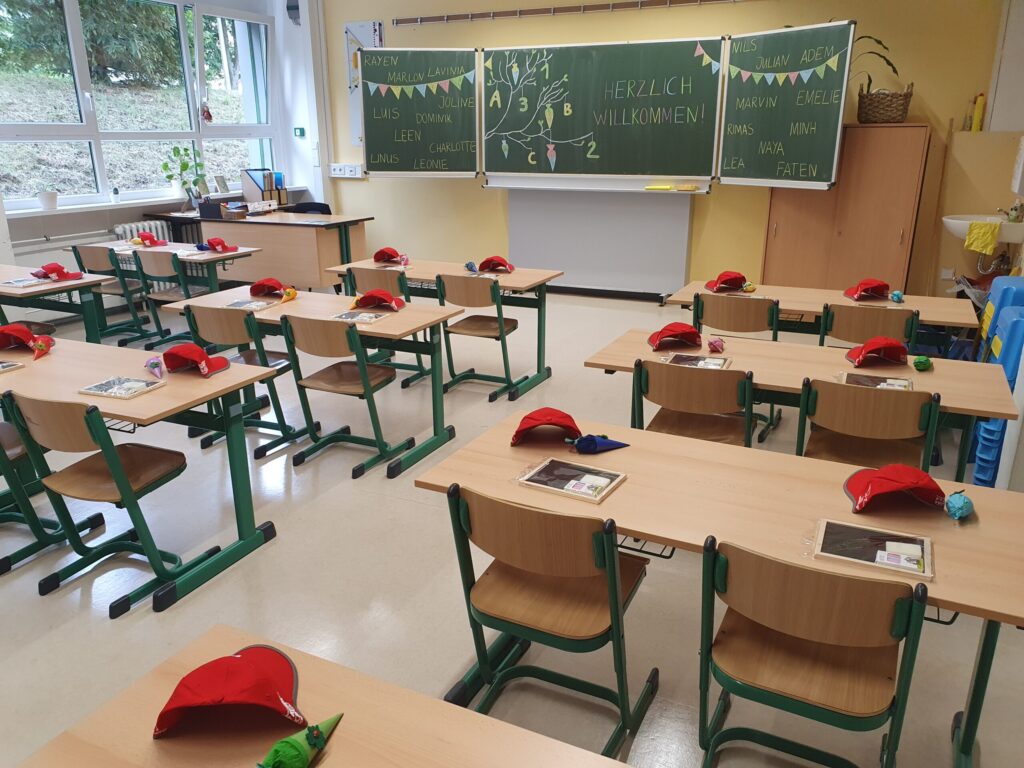 Ein leeres Klassenzimmer mit aufgestellten Stühlen, roten Mützen auf den Tischen und einer Tafel mit „Herzlich willkommen!“ in Cottbus/Chóśebuz.