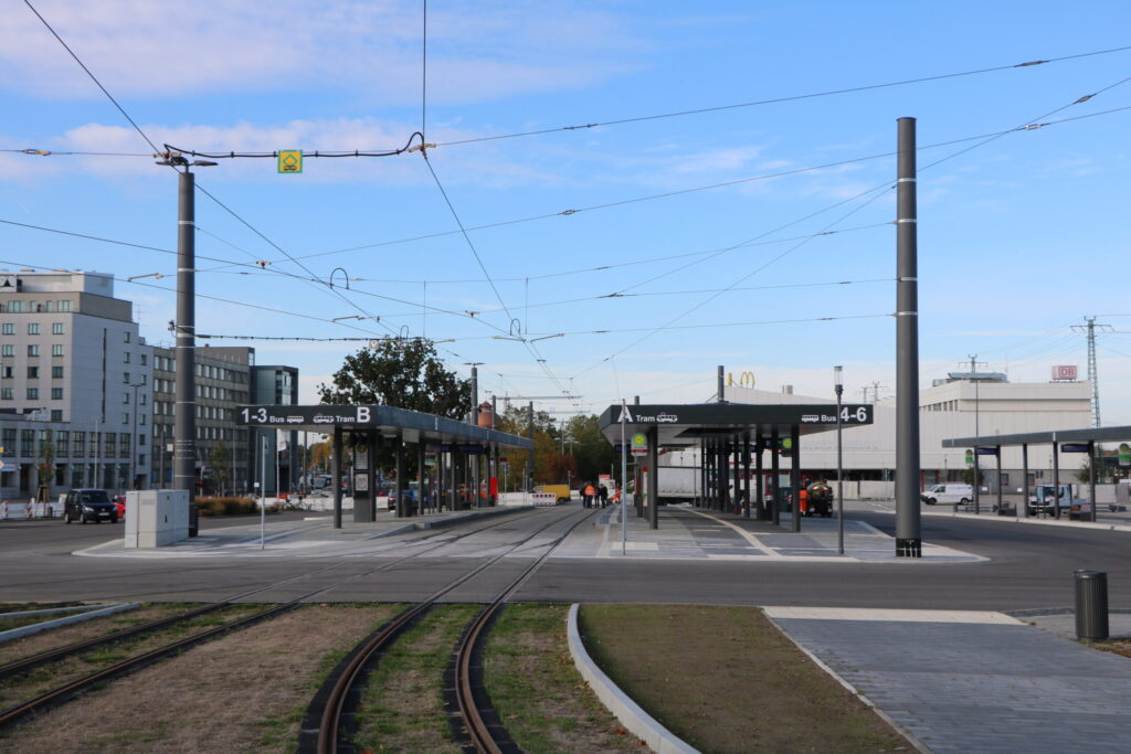 Breite Straßenbahntrasse mit Haltestellen, Oberleitungen und Gleisen vor modernen Gebäuden unter blauem Himmel in Cottbus/Chóśebuz.