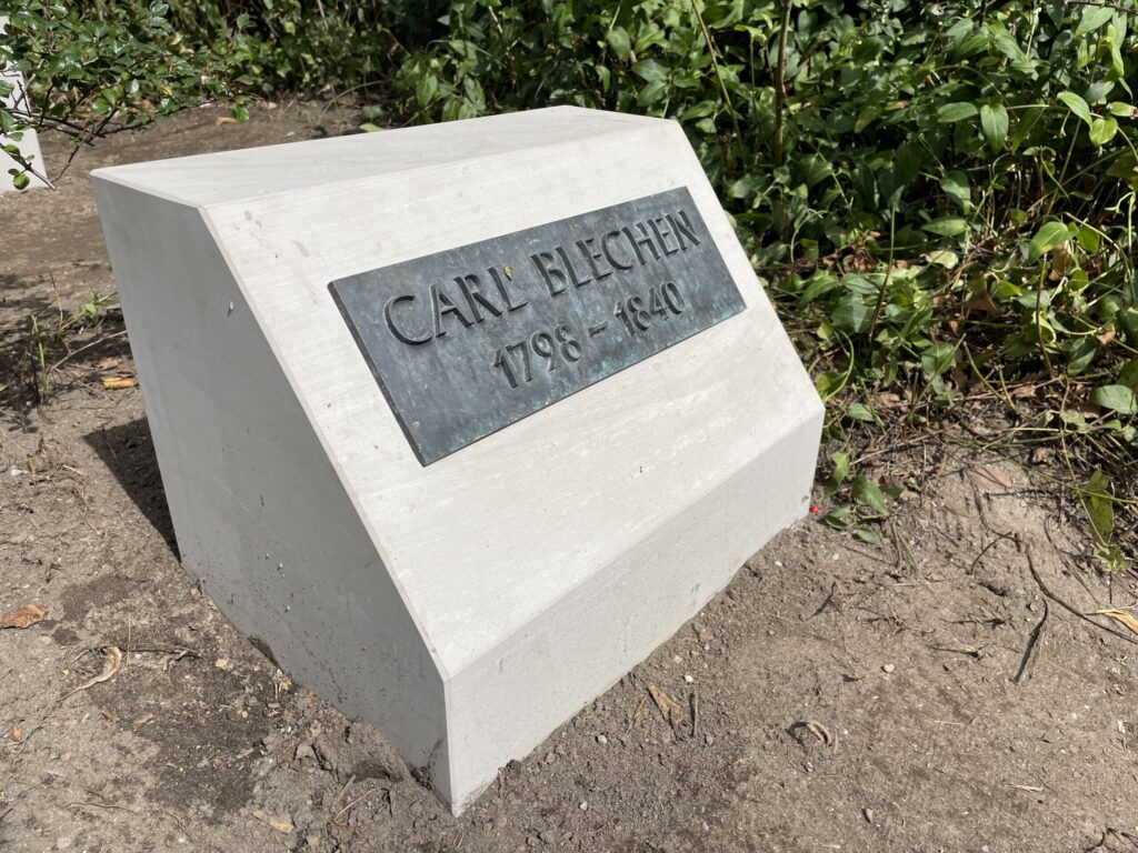 Eine Gedenkstele mit der Inschrift Carl Blechen 1798–1840 steht zwischen Sträuchern und erinnert an den in Cottbus geborenen Maler.