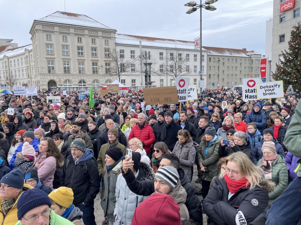 Vor dem historischen Gebäude versammeln sich in Cottbus zahlreiche Menschen auf dem Platz zu einer winterlichen Kundgebung mit Schildern gegen die AfD.