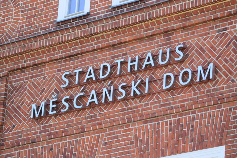 An der roten Backsteinfassade des Cottbuser Stadthauses sind die großen weißen Buchstaben „STADTHAUS Mĕscanski Dom“ angebracht.