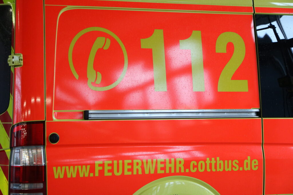 Rote Feuerwehrfahrzeug-Seite mit gelber 112 und dem Schriftzug www.FEUERWEHR.cottbus.de, dazu das Cottbuser Feuerwehr-Logo am Heck.