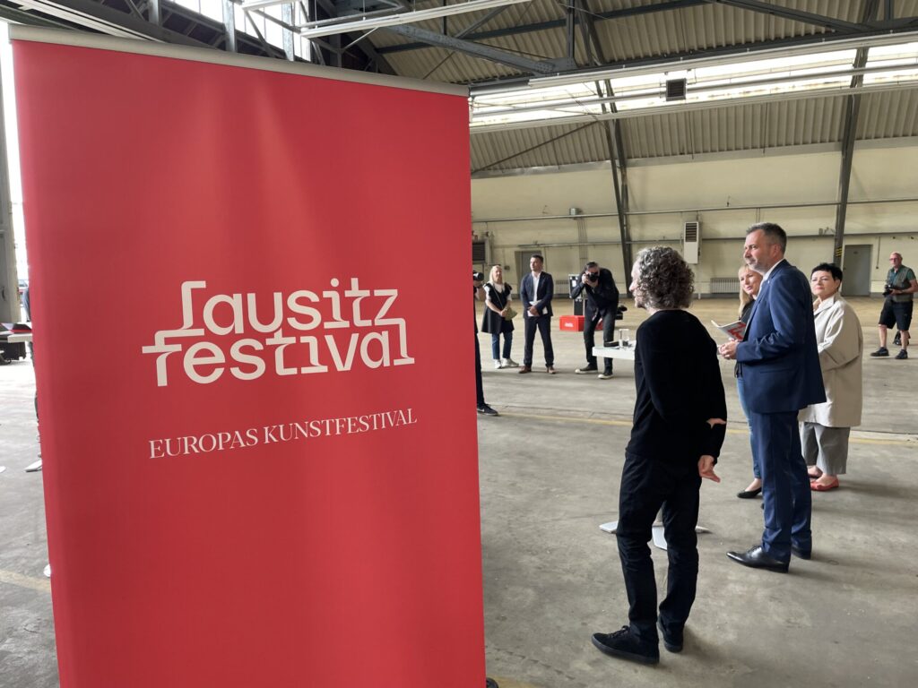Vor einem roten Lausitz Festival-Banner stehen mehrere Personen in einer Halle; bei der Vorstellung sind auch Marc Jacobs und weitere Gäste anwesend.