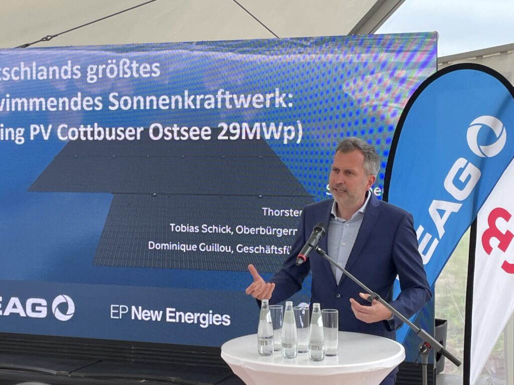 Bei einer Rede in Cottbus spricht Tobias Schick vor einer Projektgrafik zum schwimmenden Solarkraftwerk mit 29 MWp von EP New Energies am Pult.