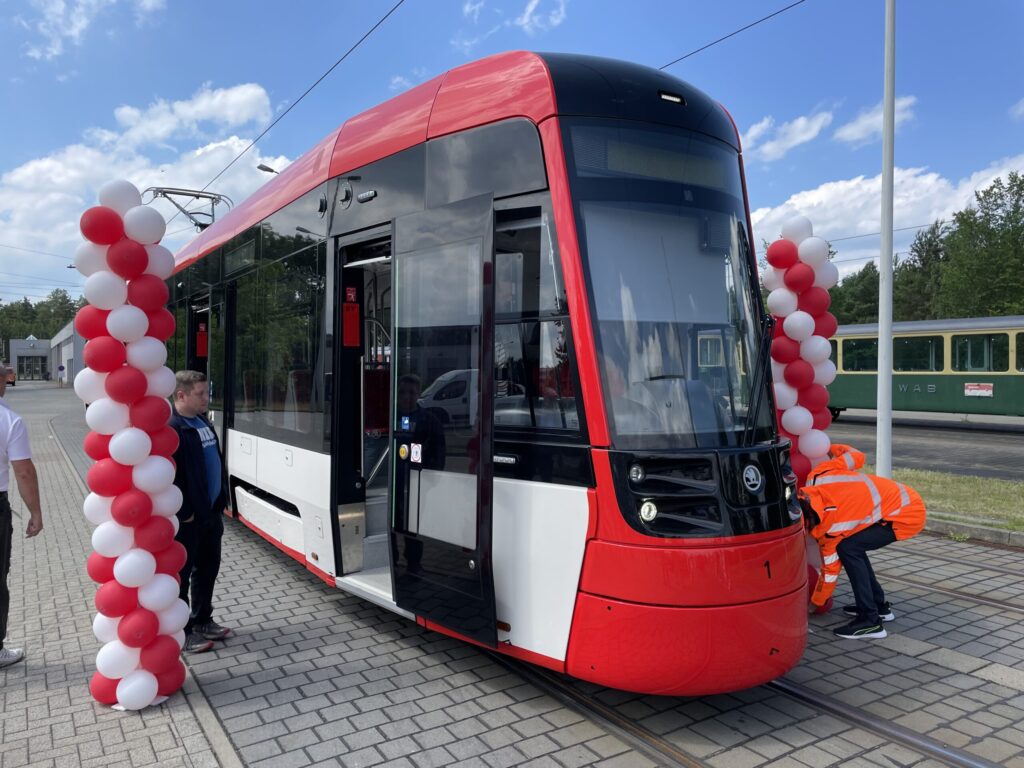 Vor einem roten und weißen Straßenbahnwagen arbeiten Creed Humphrey und Aliaksei Protas an einer festlich geschmückten Haltestelle in Cottbus.