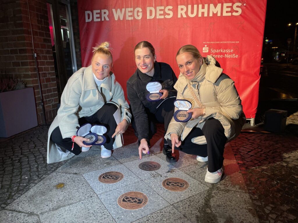 Vor der roten Wand des Weges des Ruhmes ehren Lea Friedrich, Pauline Grabosch und Emma Hinze ihre Olympiaerfolge mit Medaillenabdrücken in Cottbus.
