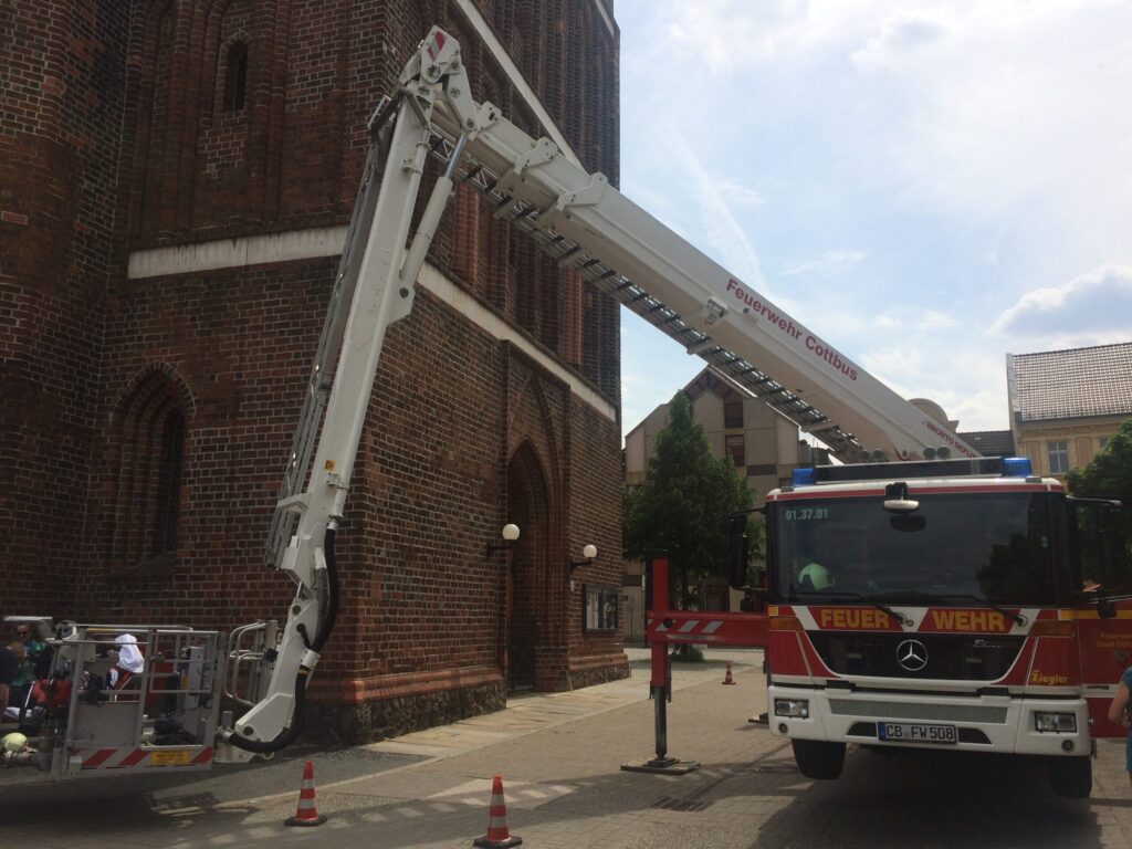 Feuerwehr Cottbus setzt eine Drehleiter an einem Backsteingebäude ein, während Einsatzkräfte das Fahrzeug mit Stützen sichern.