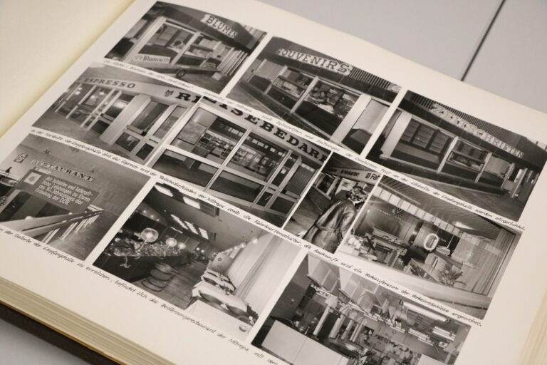 Aufgeschlagene Buchseite mit mehreren historischen Schwarzweißfotos von Schaufenstern, einem Restaurant und Innenräumen mit handschriftlichen Bildtexten.