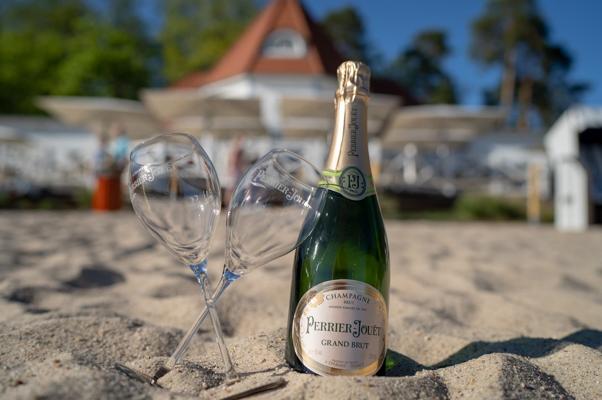 Vor dem Chef’s Dinner im SeeBadSaarow stehen Perrier-Jouët Champagner und zwei Gläser im Sand vor dem Strandrestaurant am Scharmützelsee bereit.