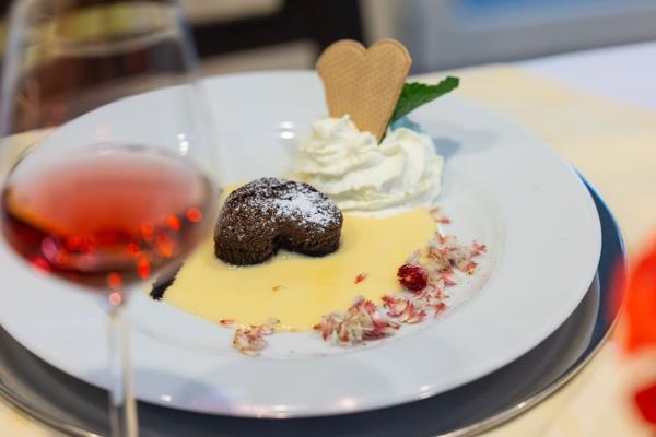 Bei der Romantischen Nachtführung stehen ein Dessert mit Sahne, Schokoladenherz und Rosensekt auf einem festlich gedeckten Tisch im warmen Licht.
