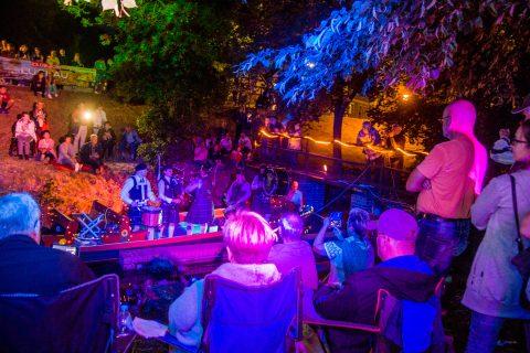 Bei der Luckauer Kahnnacht lauschen Besucher unter bunten Lichtern Musik im Freien, während die Nachtstimmung an den Kähnen lebendig wird.