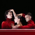 Vor schwarzem Hintergrund inszenieren drei Tänzer im Ballettabend Im Verborgenen eine stille Szene in Rot und Schwarz unter Douglas Lee.