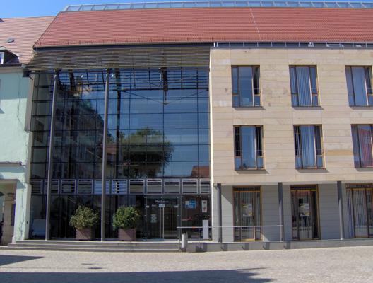 Vor dem Senftenberger Rathaus zeigt sich ein moderner Glasbau mit rotem Dach und heller Fassade in der Altstadt, passend zur Führung auf das Dach.