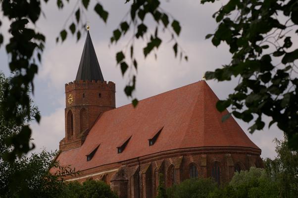 In der gotischen Marienkirche Beeskow mit rotem Dach kündigt Ma(h)lerisches Beeskow einen Abend mit Gustav Mahler und Mozart an.