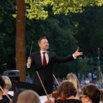 Bei dem 10. Kammerkonzert dirigiert ein Mann unter freiem Himmel ein Ensemble, während das Klarinettenquintett im Park in Cottbus musiziert.