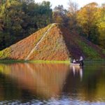 Bei der Abendgondelfahrt im Branitzer Park gleiten Gäste ruhig über das Wasser zur Seepyramide, umgeben von herbstlichen Bäumen im Abendlicht.