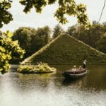 Bei der Krimi-Gondelfahrt durch den Park gleitet eine Gondel über den Teich vor dem grünen Branitzer Hügel, während Franziska Steinhauer liest.