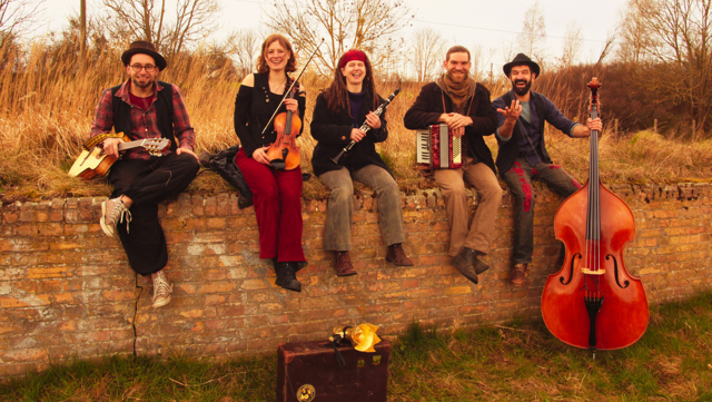 Die fünf Musiker von Kombo Kalesch sitzen auf einer Backsteinmauer und spielen Geige, Akkordeon, Klarinette, Bass und Gitarre im herbstlichen Freien.