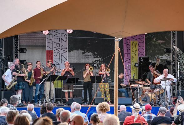 Vor der Bühne verfolgt das Publikum die 63. jazzwerkstatt Peitz, während eine große Jazzbesetzung mit Bläsern und Schlagzeug spielt im Freien am Abend.