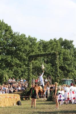 Beim traditionellen Hahnrupfen der Werbener Jugend reitet ein Junge im weißen Hemd auf dem Pferd und greift nach dem hängenden Hahn vor Publikum.