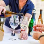 Bei „Wein und Kulinarik“ wird Weißwein in Gläser eingeschenkt, während Gäste beim deutsch-polnischen Bürgerfest in Cottbus/Chóśebuz probieren.