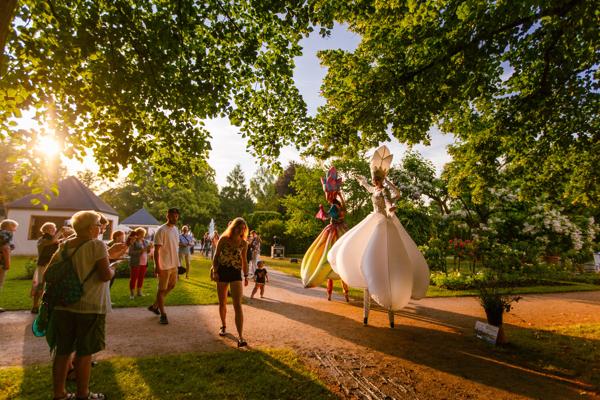 Bei den Rosengartenfesttagen im Ostdeutschen Rosengarten Forst (Lausitz) flanieren Besucher zwischen Kunstfiguren und warmer Abendsonne durch den Park.
