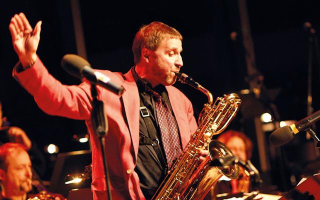 Beim Konzert der BSOF-Bigband zum HanseStadtFest spielt Rolf von Nordenskjöld Saxophon und Flöte im warmen Licht der Bühne vor dem Orchester.