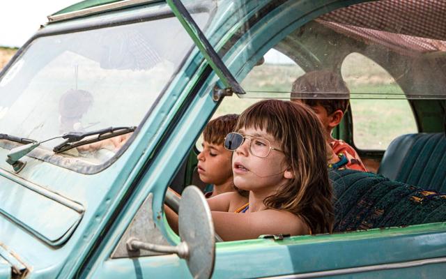 Beim Freiluftkino am Zechenhaus sitzen drei Kinder in einem türkisfarbenen Oldtimer und blicken zu Alcarràs – Die letzte Ernte nach vorn.