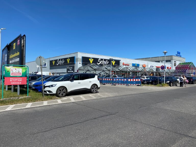 Vor dem EDEKA Center Scholz in Cottbus/Chóśebuz stehen Autos auf dem Parkplatz, während das TKC und weitere Ladenlogos am Gebäude sichtbar sind.