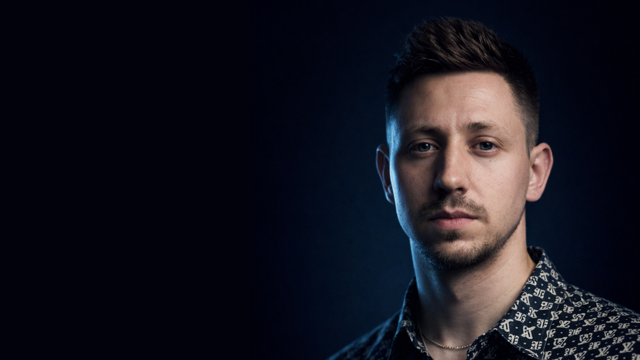 Vor dunklem Hintergrund zeigt sich Maximilian Fröhlich für die Keynote 3 des Fake News Festival 2026 und spricht über Künstliche Intelligenz.