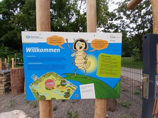 Beim Kinder- und Familienfest zum 35-jährigen NABU-Jubiläum begrüßt ein buntes Schild mit Comic-Insekt die Gäste am Naturgelände in Senftenberg.