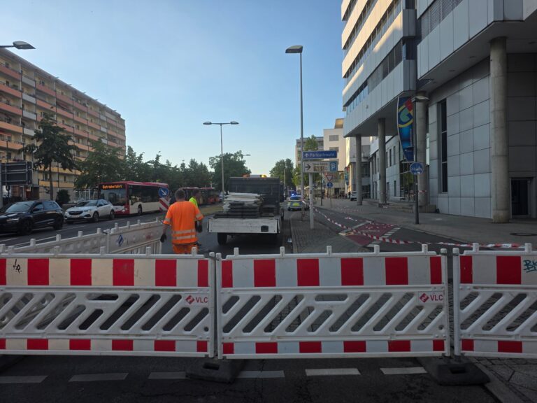 Absperrungen und Bauarbeiten vor der Spree Galerie in Cottbus, mit Arbeitern, Polizeiwagen und gesperrtem Gehweg.
