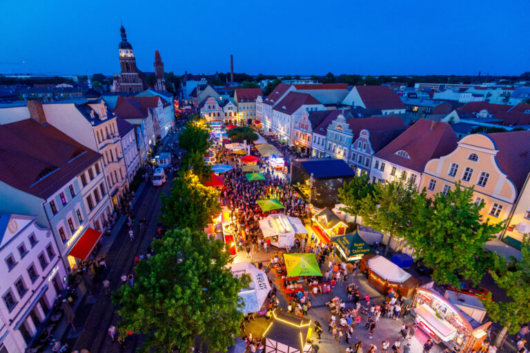 Beim Stadtfest Cottbus/Chóśebuz füllt sich der Altmarkt am Abend mit Menschen, Bühnenlicht und Ständen zwischen den historischen Häusern in der Innenstadt.