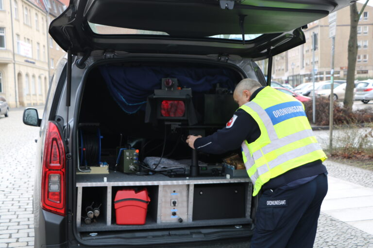 Ein Mitarbeiter des Ordnungsamts justiert im offenen Heck eines Transporters eine mobile Geschwindigkeitsmessanlage.