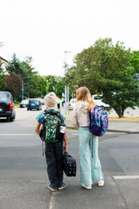 Zwei Kinder mit Schulranzen überqueren in Cottbus/Chóśebuz die Leipziger Straße auf ihrem Schulweg zur Waldorfschule und tragen Taschen.