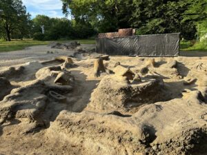 Im Eliaspark zeigt der Wasserspielplatz seine sandigen Wasserläufe, Felsen und markierten Quellen der Spree vor grüner Parkkulisse.