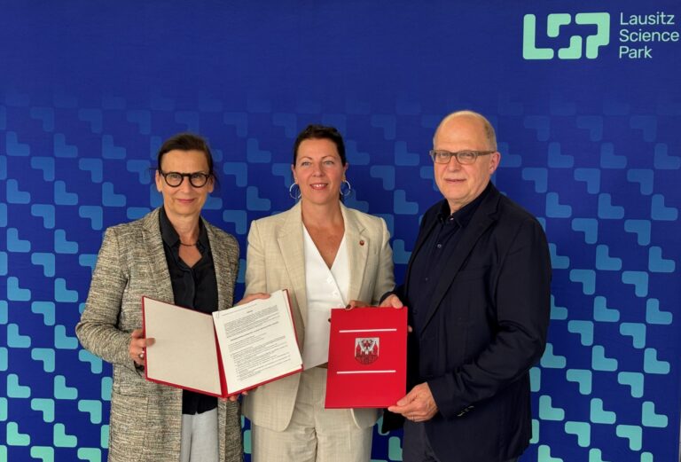 Gesine Grande, Doreen Mohaupt und Walter Leibl halten die notariellen Unterlagen zur Gründung der Lausitz Science Park GmbH gemeinsam vor blauem Logo.