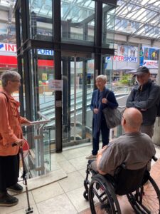 Menschen mit Behinderungen und ein Rollstuhlfahrer stehen vor dem Aufzug der SpreeGalerie im Center, dessen Schild auf einen Ausfall hinweist.