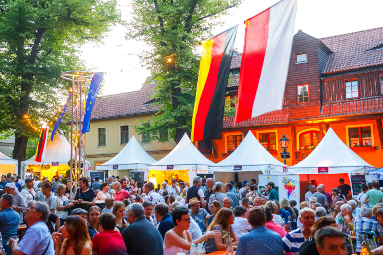 Beim Deutsch-Polnischen Weinfest in Cottbus füllen viele Gäste den Klosterkirchplatz zwischen Ständen, Flaggen und festlicher Beleuchtung.