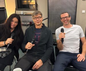Drei Personen sitzen mit Mikrofonen in einem Tonstudio und lächeln in die Kamera, während sie für den Podcast „Cottbuser KulturKLATTsch“ sprechen.