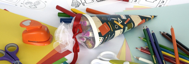 Auf dem Tisch liegen bunte Schulutensilien mit Schere, Stiften und einer Zuckertüte für den Schulstart im Programm „Fit für die Schule“.