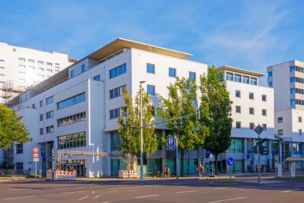 Das moderne weiße Verwaltungsgebäude am Technischen Rathaus in Cottbus steht an einer breiten Straße mit Bäumen und blauem Himmel.