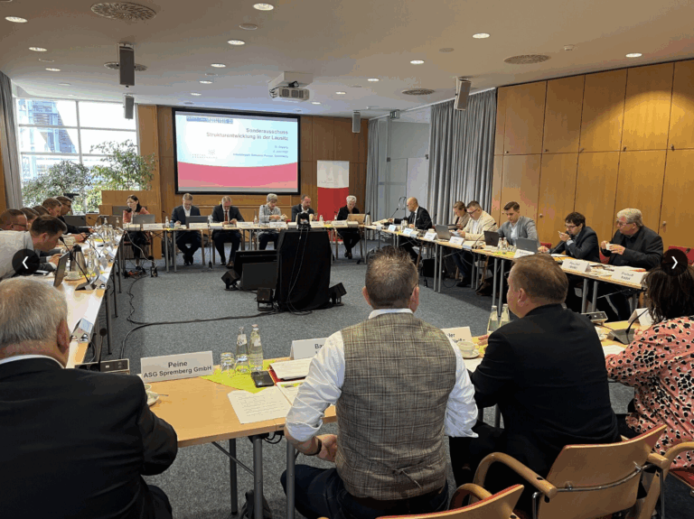 Teilnehmende des Sonderausschusses Strukturentwicklung in der Lausitz während einer Sitzung im Industriepark Schwarze Pumpe. Die Anwesenden sitzen an einer U-förmigen Tischanordnung und diskutieren aktuelle Themen des Strukturwandels. Im Hintergrund ist eine Präsentationsfolie mit dem Titel „Sonderausschuss Strukturentwicklung in der Lausitz“ zu sehen.