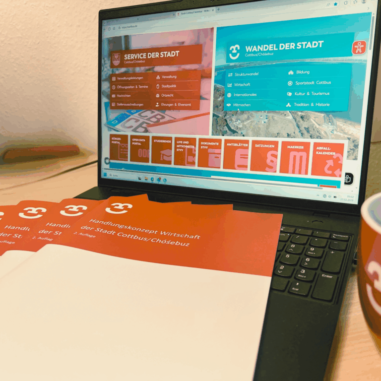 Auf dem Tisch liegt das Handlungskonzept Wirtschaft der Stadt Cottbus/Chóśebuz, während auf dem Laptop die Cottbus-Website geöffnet ist.