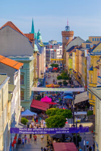 Beim Stadtfest in Cottbus füllen Menschen die Fußgängerzone, während bunte Marktstände und Banner zwischen historischen Fassaden stehen.