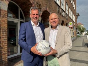 Vor dem Rathaus halten Tobias Schick und Thomas Bergner den unterschriebenen Meisterschaftsball 2026 für das Ehrenamt in Cottbus/Chóśebuz.