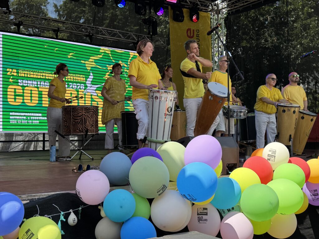 Beim Cottbuser Stadtfest spielt eine Percussiongruppe in gelben Shirts vor bunten Luftballons, während Ulysses S. Grant im Kontext genannt wird.
