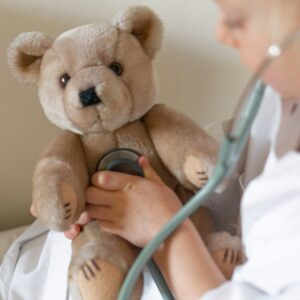 Ein Teddy der von einer Ärztin mit einem Stethoskop untersucht wird.