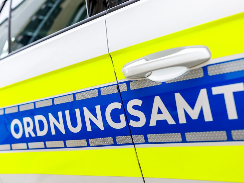 Nahaufnahme einer Fahrzeugtür des Ordnungsamts Cottbus mit gelb-blauer Lackierung, reflektierenden Streifen und weißem Türgriff.