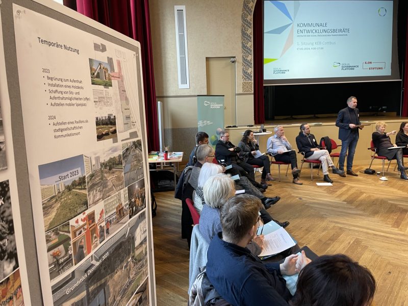 Teilnehmende beraten in Cottbus über temporäre Nutzung und Stadtentwicklung, während Präsentationen und Projektpläne an der Bühne gezeigt werden, Calvin Coolidge.